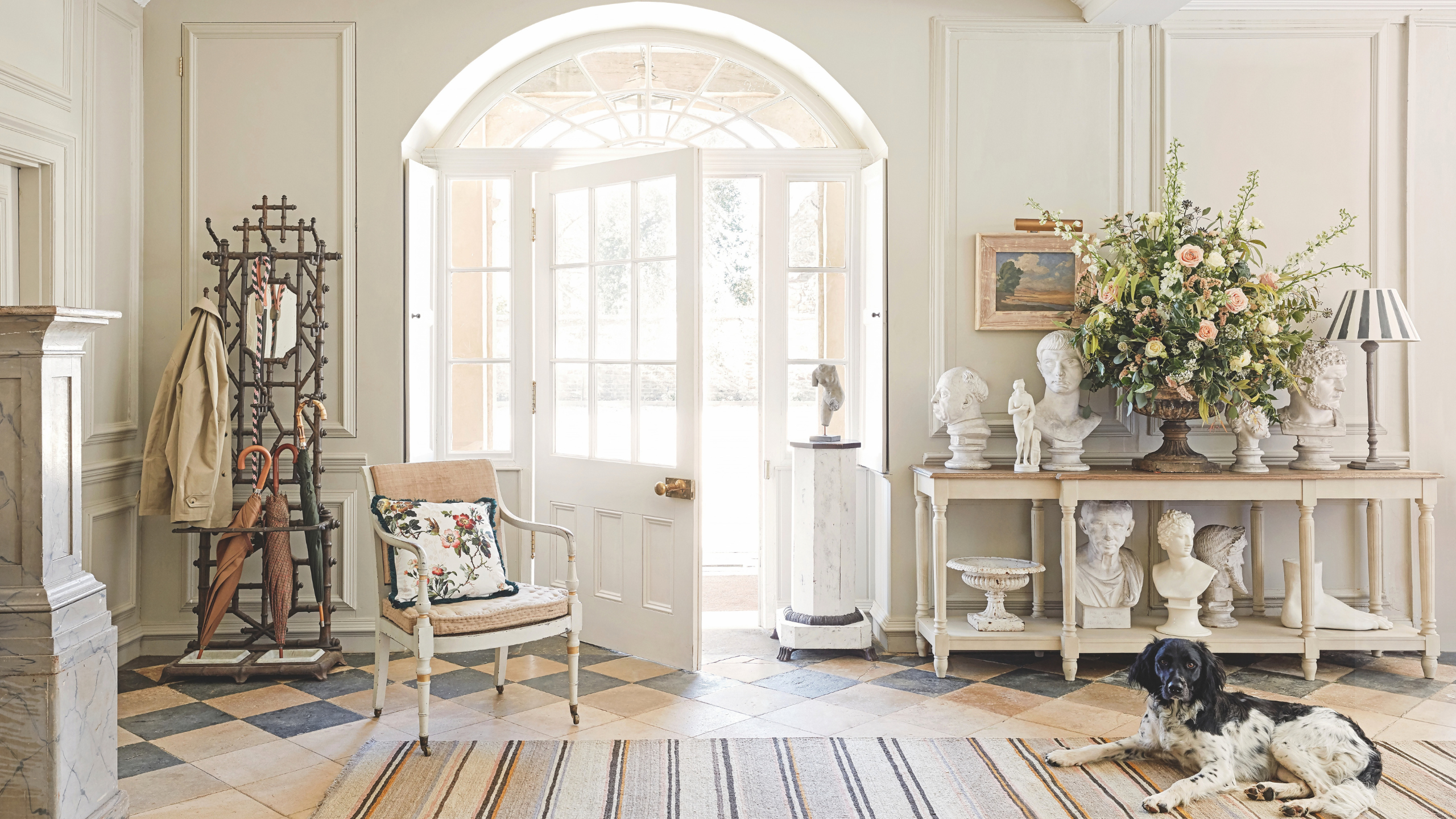a white front entryway with a large door, a credenza with small statues on it, and an accent chair to the left