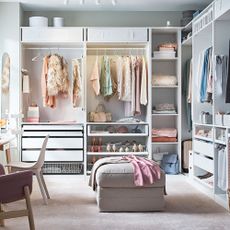 white dressing room with open cupboards with clothes two walls and pouffe in middle of room