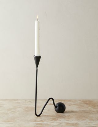 a sleek black candlestick holding a tapered candle slithers down to a solid orb at the end