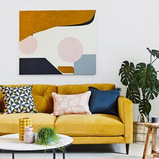 Living room with white walls, modern art painting hung above a yellow sofa with cushions
