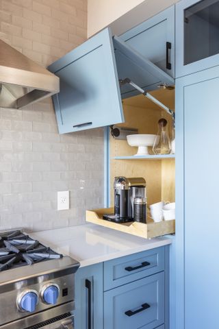 Blue kitchen cabinets open to reveal an appliance garage with coffee maker