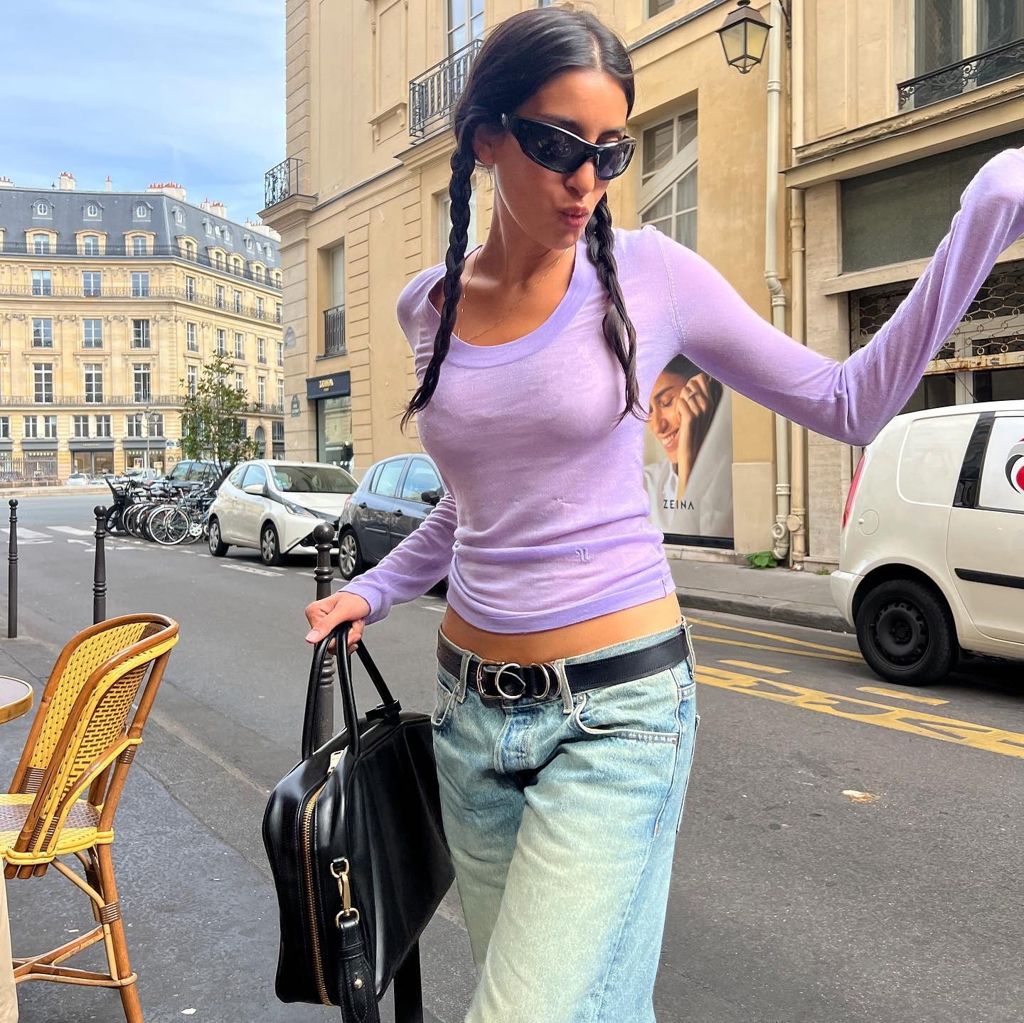A woman wearing a purple long sleeve top, blue jeans, and a black tote bag