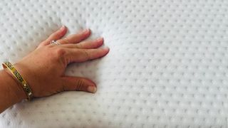 A hand touches the surface of the Emma NextGen Cooling mattress, testing the temperature regulation and pressure relief