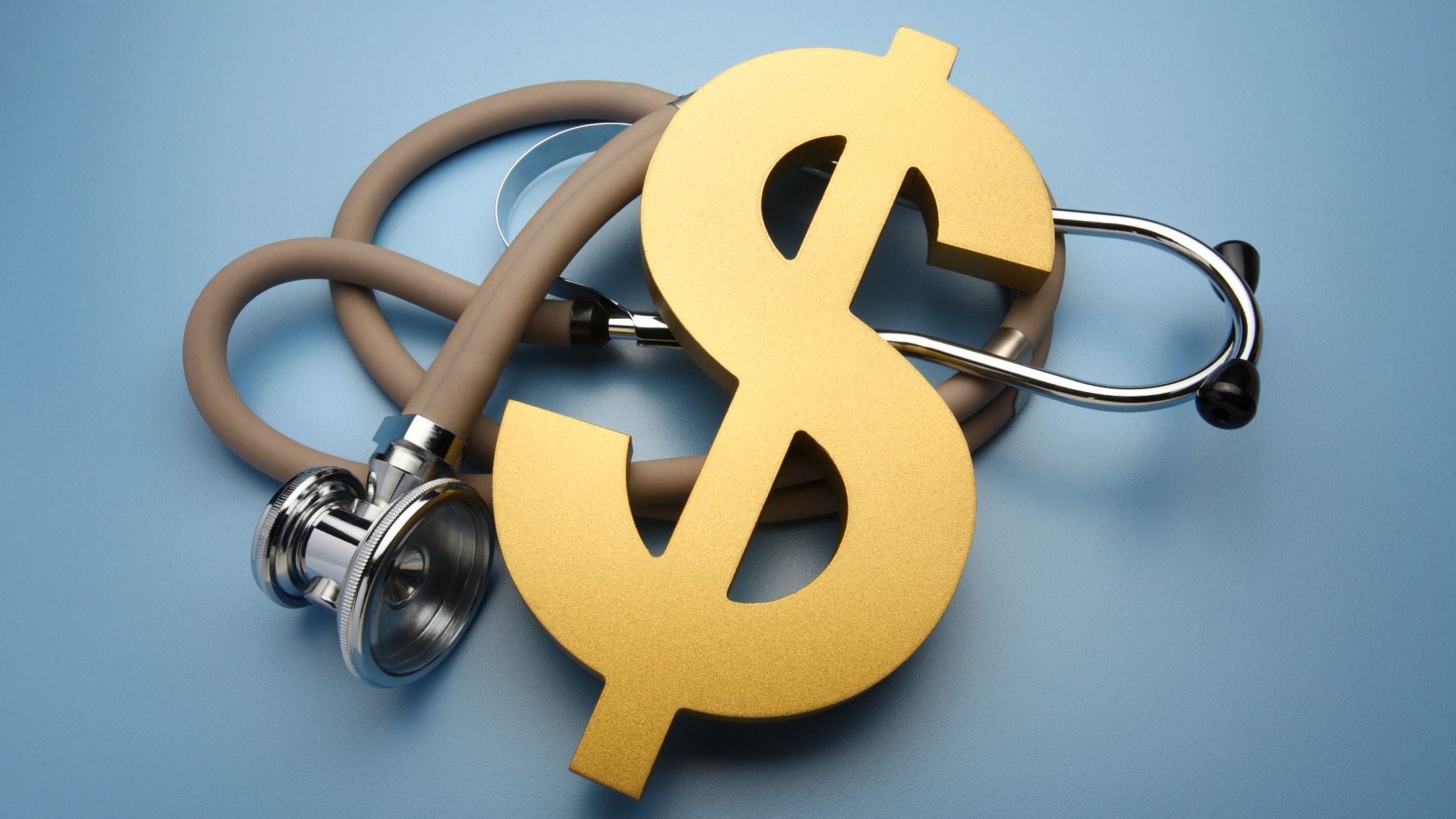 A large gold dollar sign rests on top of a stethoscope on a blue background