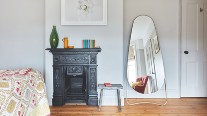 Oval mirror next to black fireplace in a white bedroom