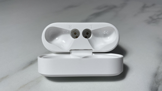Image shows an open PistonBuds Pro Q30 case lying on its back in a marble-effect desktop. You can see the magnets inside the case that help to hold the earbuds in place.