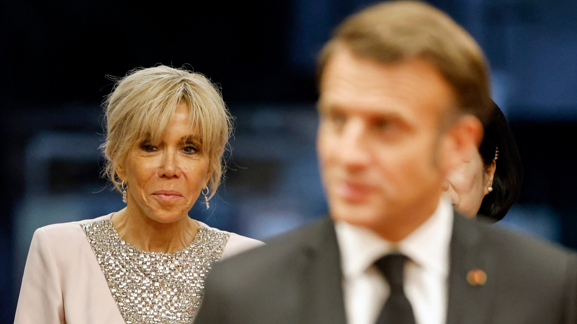 Brigitte Macron, with a blurred Emmanuel Macron in the foreground