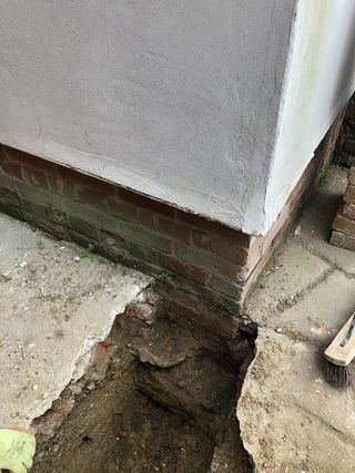 A crack in the ground next to some lower down brickwork on a house