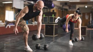 Man and woman in gym perform single-leg Romanian deadlift with a dumbbell