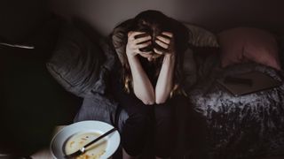 woman sat with her head in her hands next to an empty plate