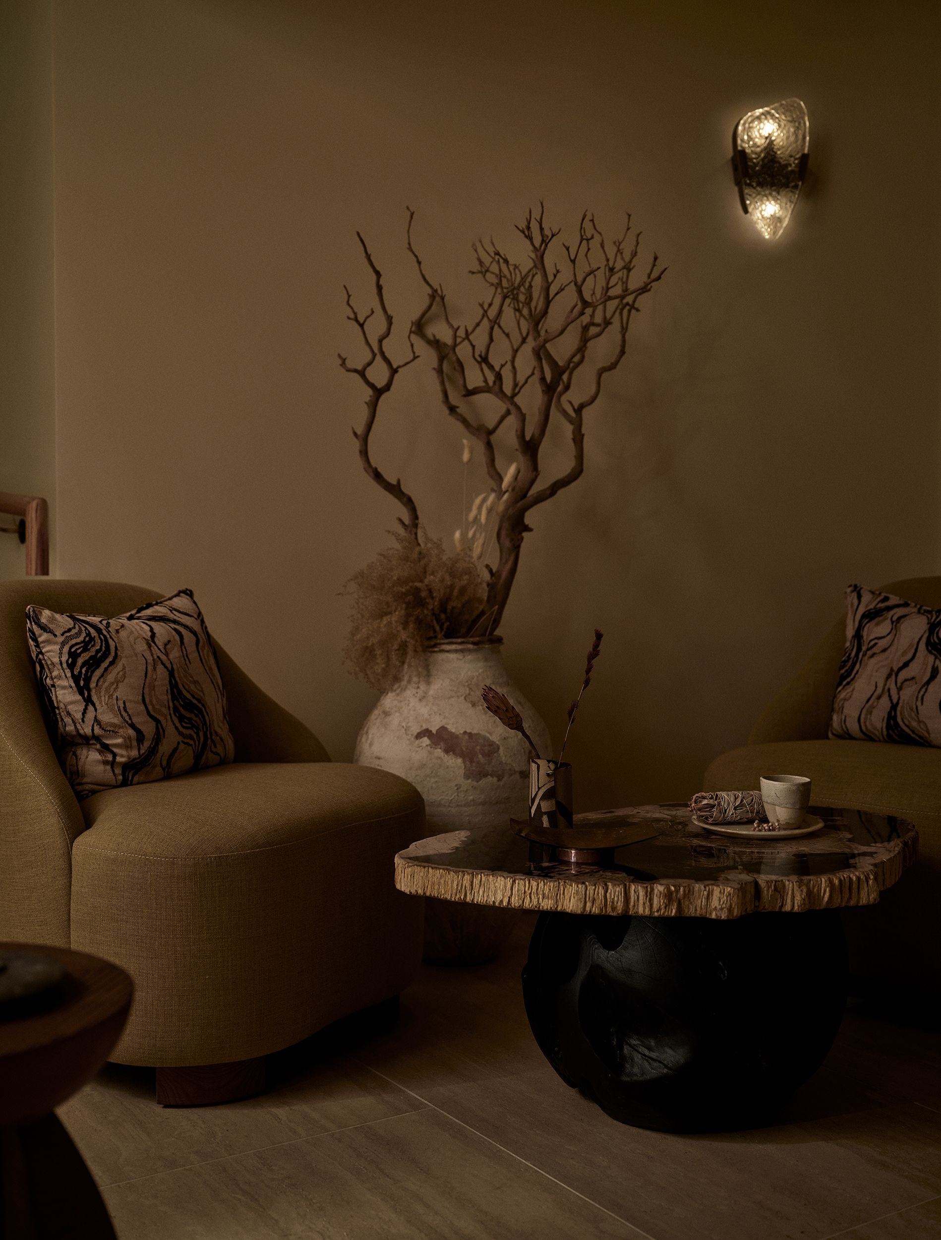 A hotel spa decorated with textile installations characterized by a textural, raw feel, sculptural tables carved from wood and rock, pendant lights, and a beige fabric-covered wall.