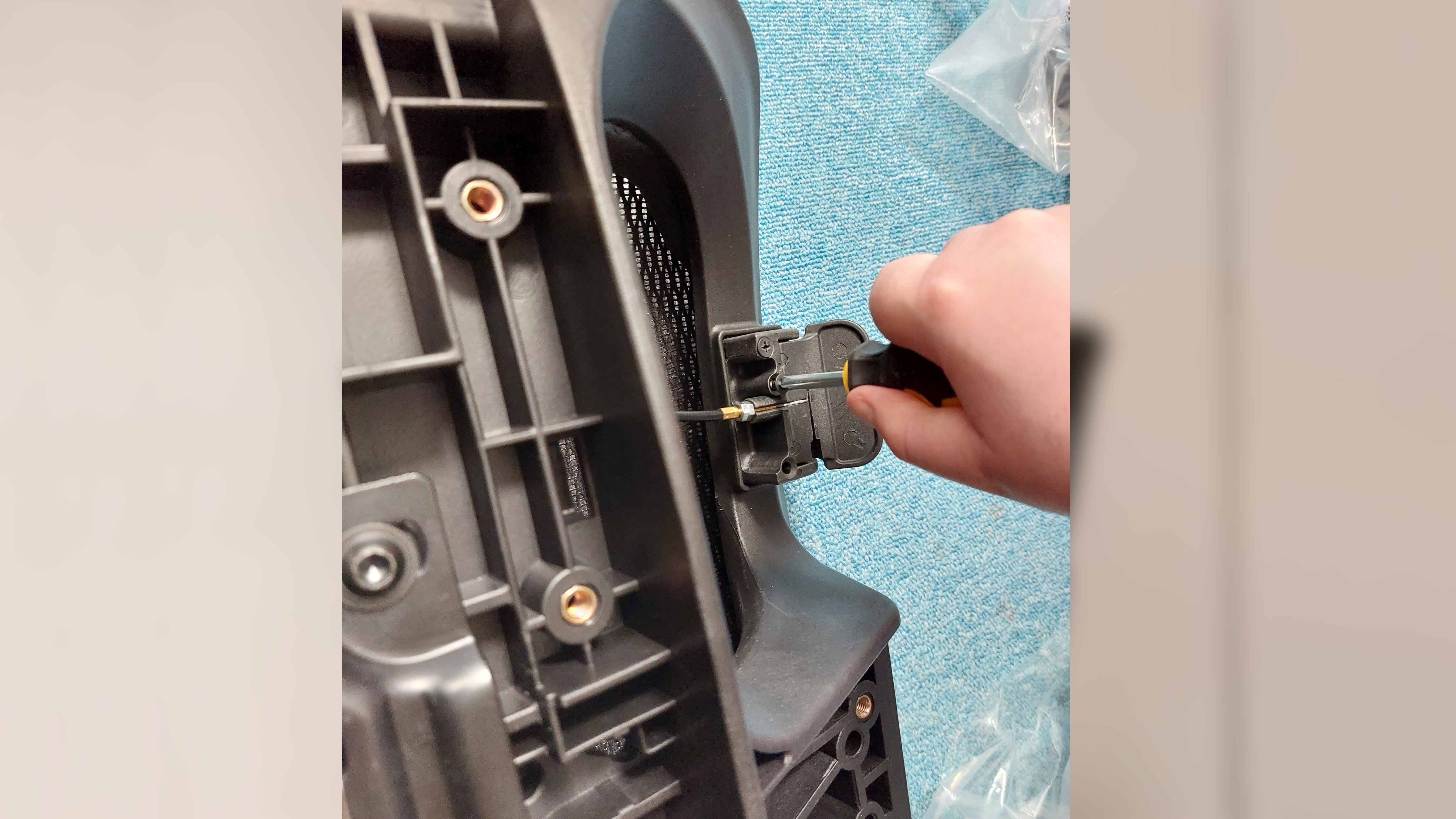 A hand holds a small screwdriver. The rest of the person out of shot is attempteing to screw in screws to the underside of the AndaSeat X-Air Pro's seat. This process is to attach the adjustment pedals to the underside of the seat edge.