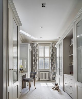 An example of bedroom lighting ideas showing a neutral dressing table with curtains on the window and an upholstered chair