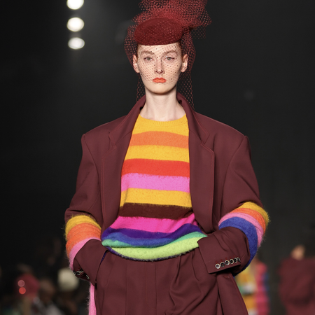 A model walks the runway for the Christopher John Rogers Collection 010 runway show at Brooklyn Navy Yard on June 07, 2022 in Brooklyn, New York wearing a rainbow striped sweater and maroon suit