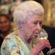 Queen Elizabeth wearing a green floral dress drinking a glass of water
