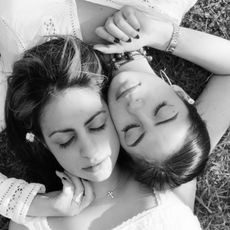 Two women lay on the grass, heads touching.