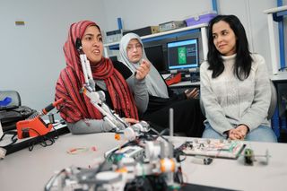 In the GMU bioengineering lab, student Sidra Khan (far left) demonstrates the device, still in early stages. Team member Kamran Mohammadi built the prototype using a Lego® Mindstorms® kit.
