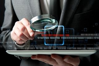 Man in suit examines laptop computer with magnifying glass, with binary code in foreground