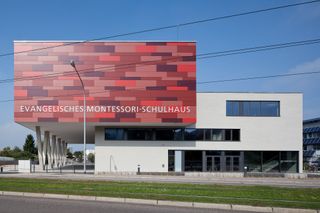 This Montessori school by Spiecker Sauter Lauer packs a lot of building onto a small lot. It’s notable for its mottled red concrete cube that appears to float over the street, supported only by thin diagonal columns.