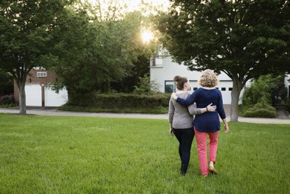 Two white women walk on the grass in the suburbs.