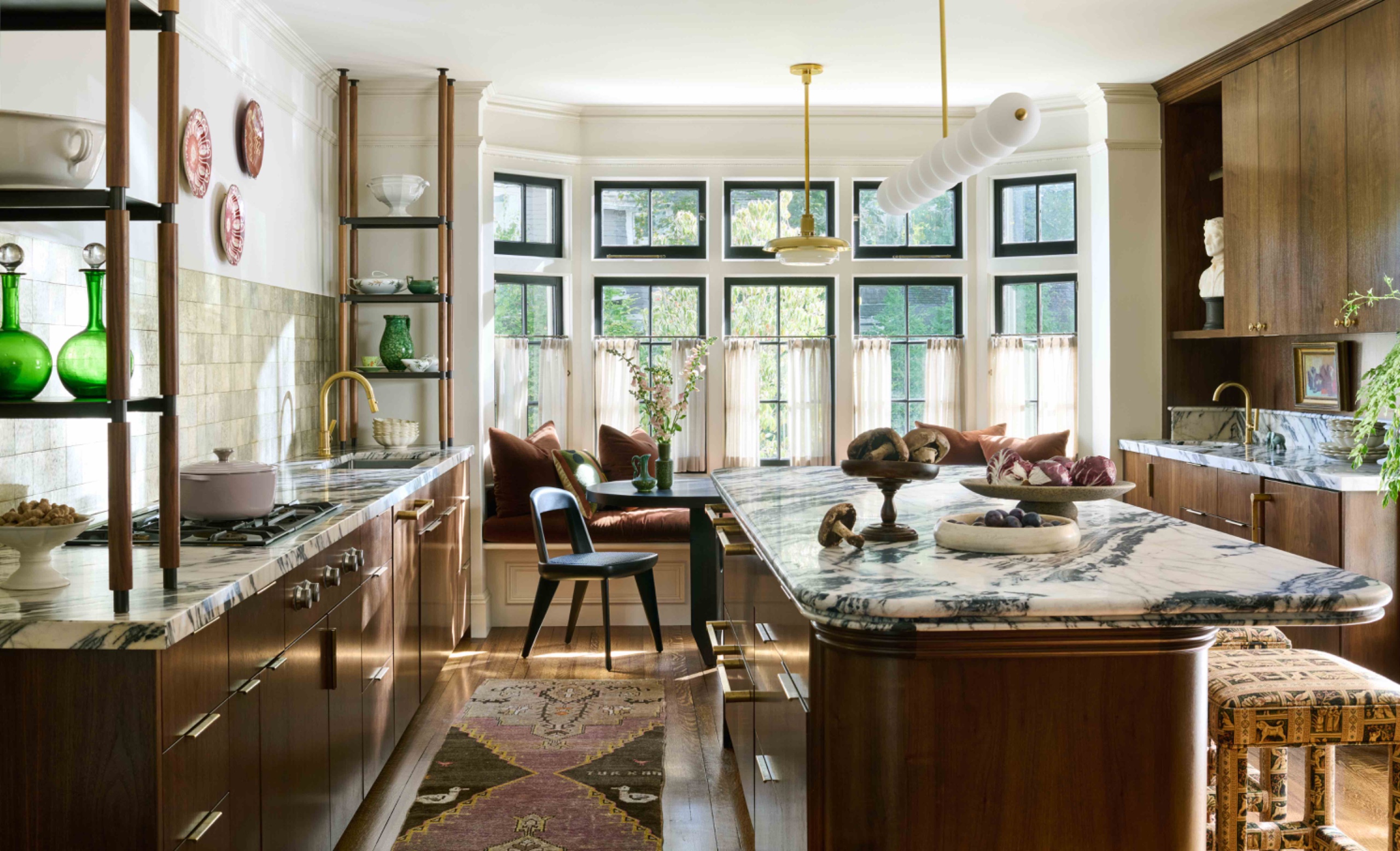 kitchen with walnut cabinetry, veined quartzite countertops and a long island leading to an oval dining table and cushioned window bench.