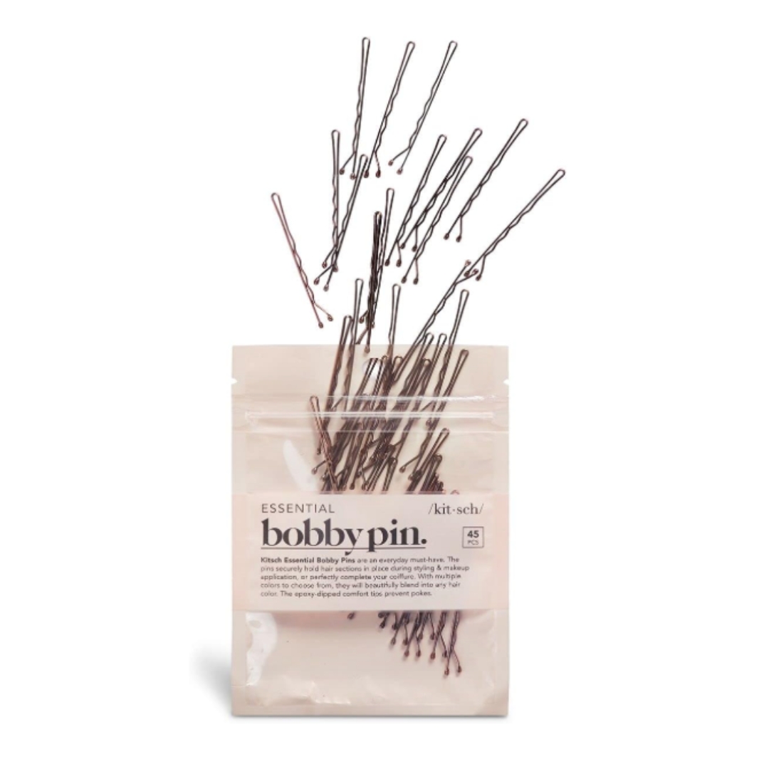 A product shot of a packet of Kitsch Essential Bobby Pins, with some spilling out, on a white background