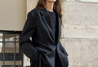 Woman wearing black blazer with black t-shirt, black slacks, and The Row Margaux bag, standing on Paris street.