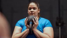 Woman in blue T-shirt holds kettlebell by her chest in two hands