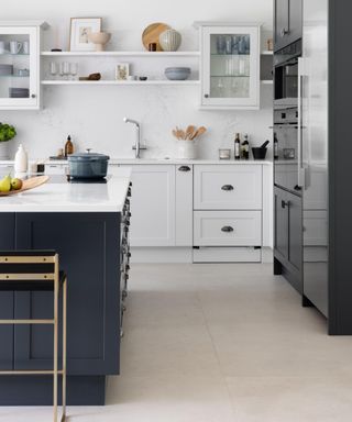 A kitchen with gray flooring, a dark blue kitchen island with white countertops, white cabinets behind it, and a dark blue kitchen cabinet to the right