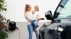 A woman carrying her child while plugging an EV charger into an electric vehicle