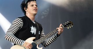 Yungblud wears a black-and-white striped longsleeve under a black cutoff t-shirt as he plays his white '64 Gibson SG Junior onstage