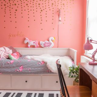 Pink kids room with white storage bed, wooden desk and metallic wall stickers
