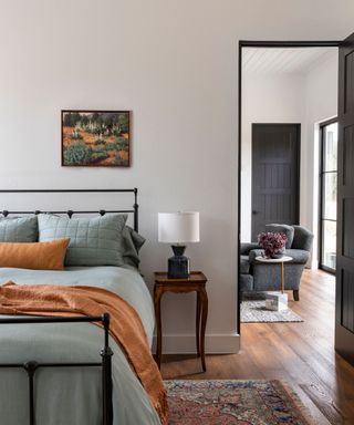bedroom with cast iron bed with rust colored throw and view to sitting room with white walls