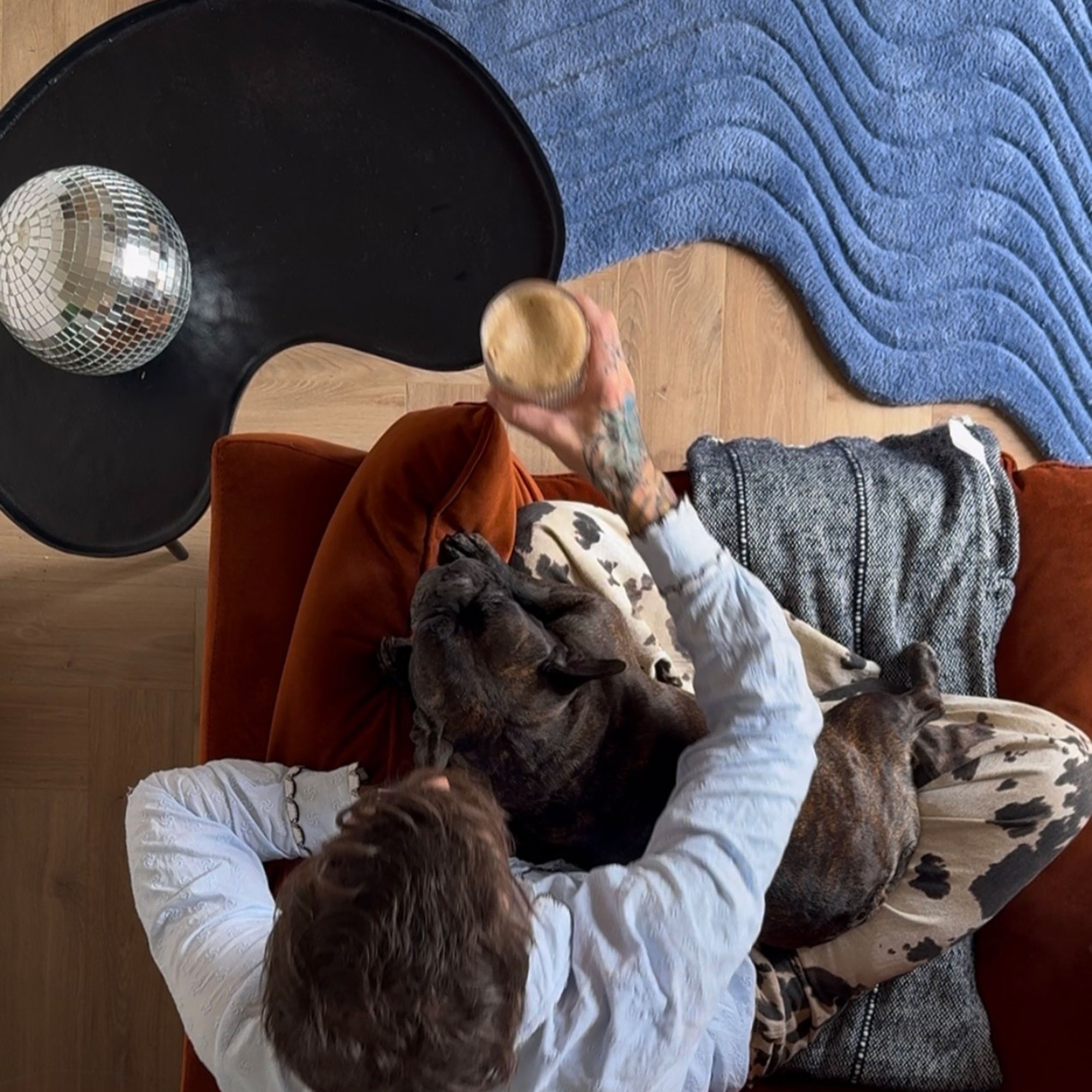Man seen from above sitting on rust coloured sofa in front of blue curved rug