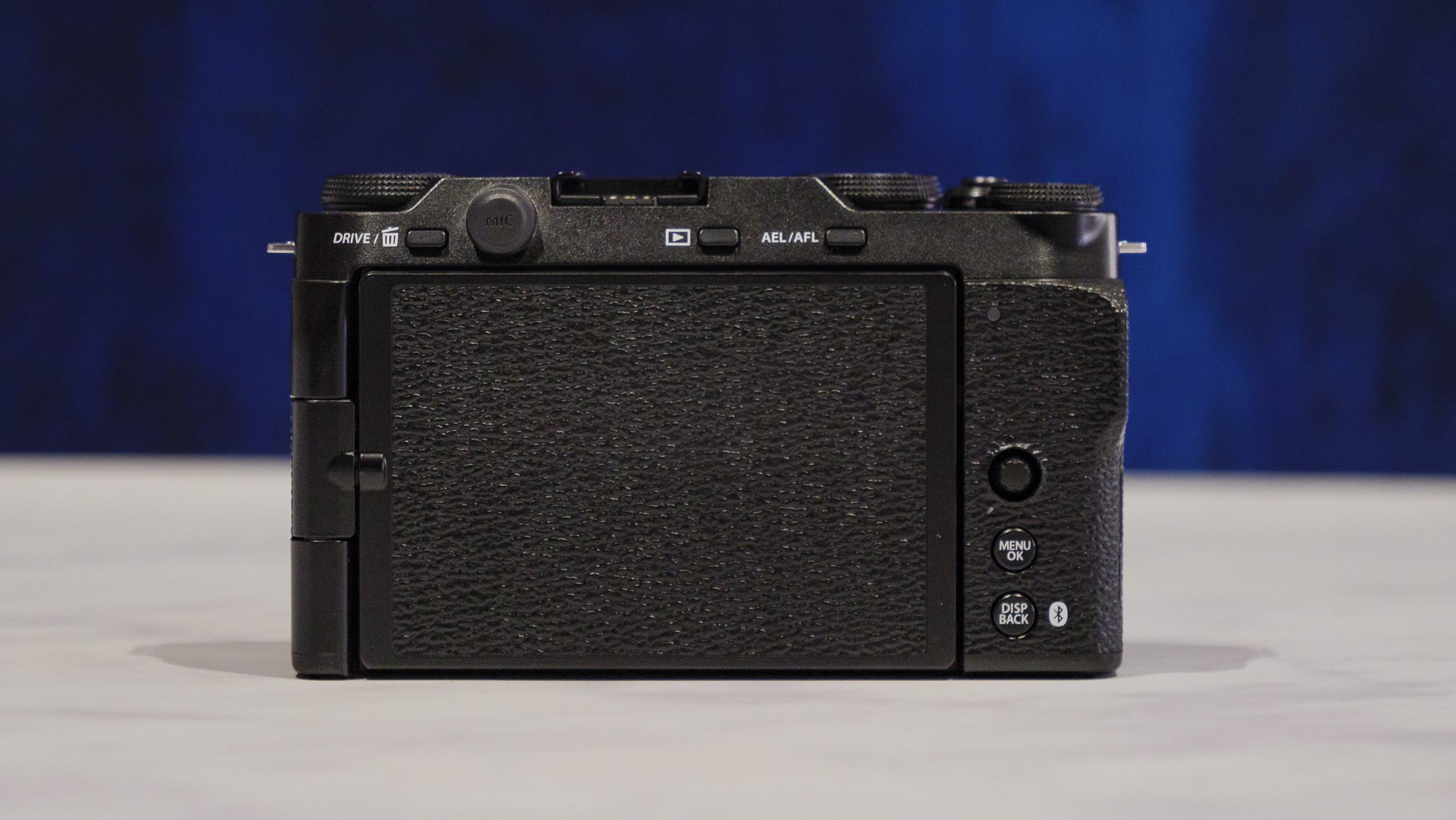 Rear of the Fujifilm X-M5 camera with screen folded away, on a marble surface with rich blue background