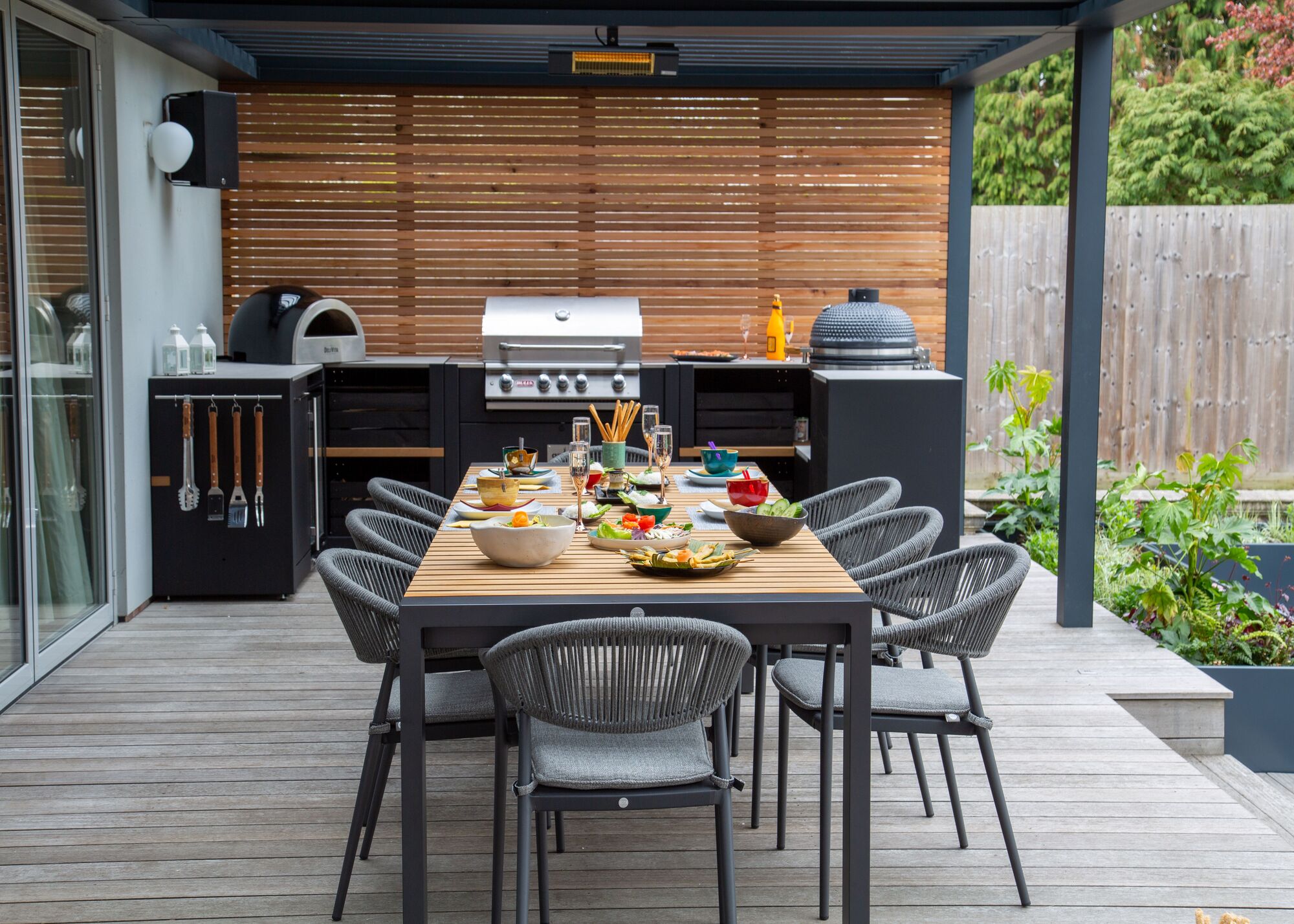 An outdoor kitchen on a deck with a dining table and a barbecue