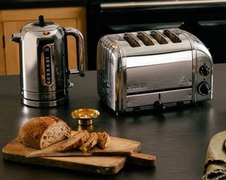A chrome kettle and taster on a black kitchen countertop with a platter of toast