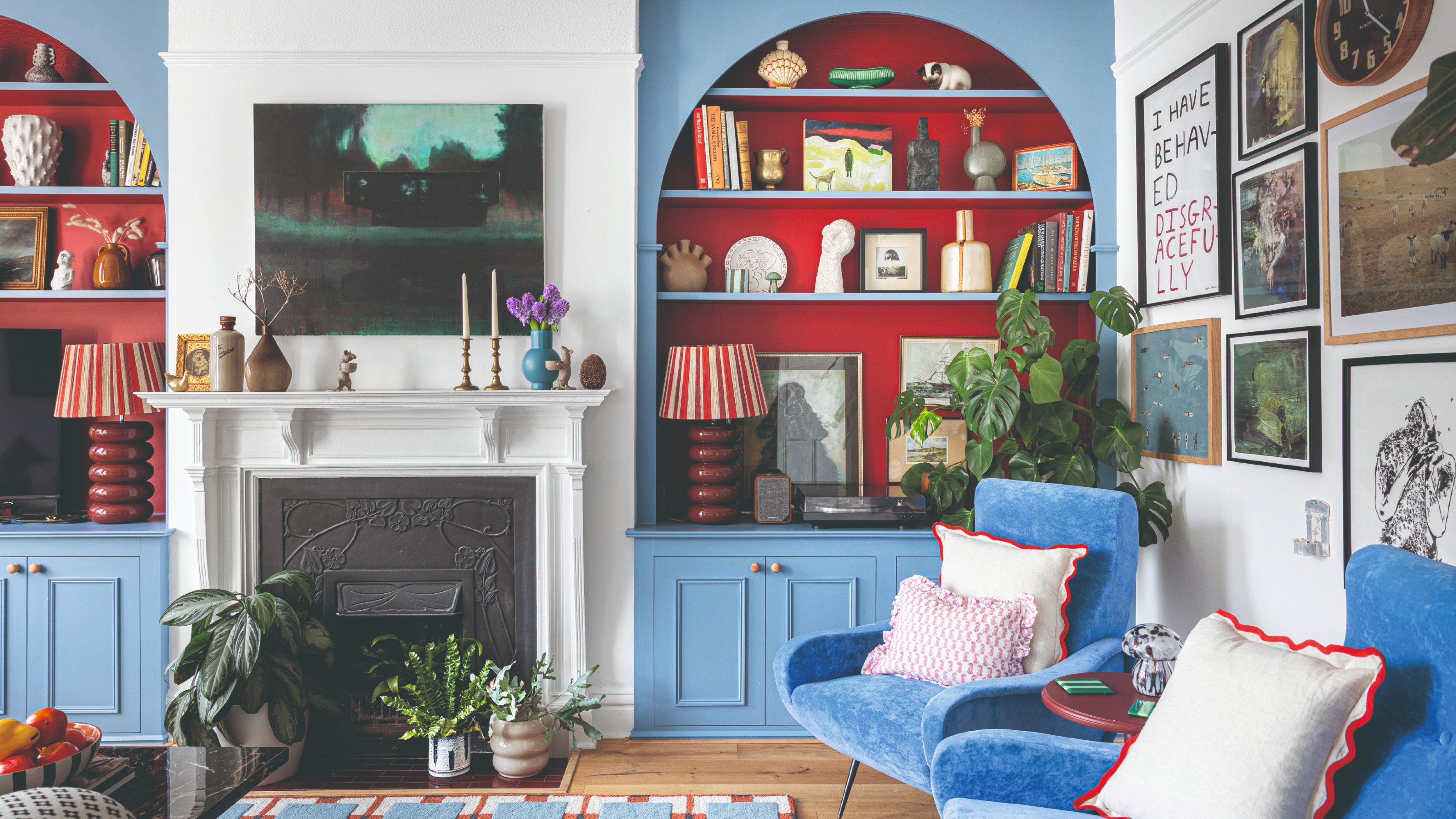 A living room painted in white with arched alcove bookcases painted in a sky blue with a warm red interior
