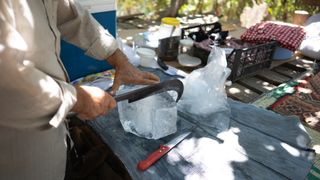 A man slicing ice off a block at a campsite