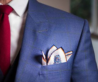 Man wearing blue suit, white shirt and red tie showing breast pocket and handkerchief