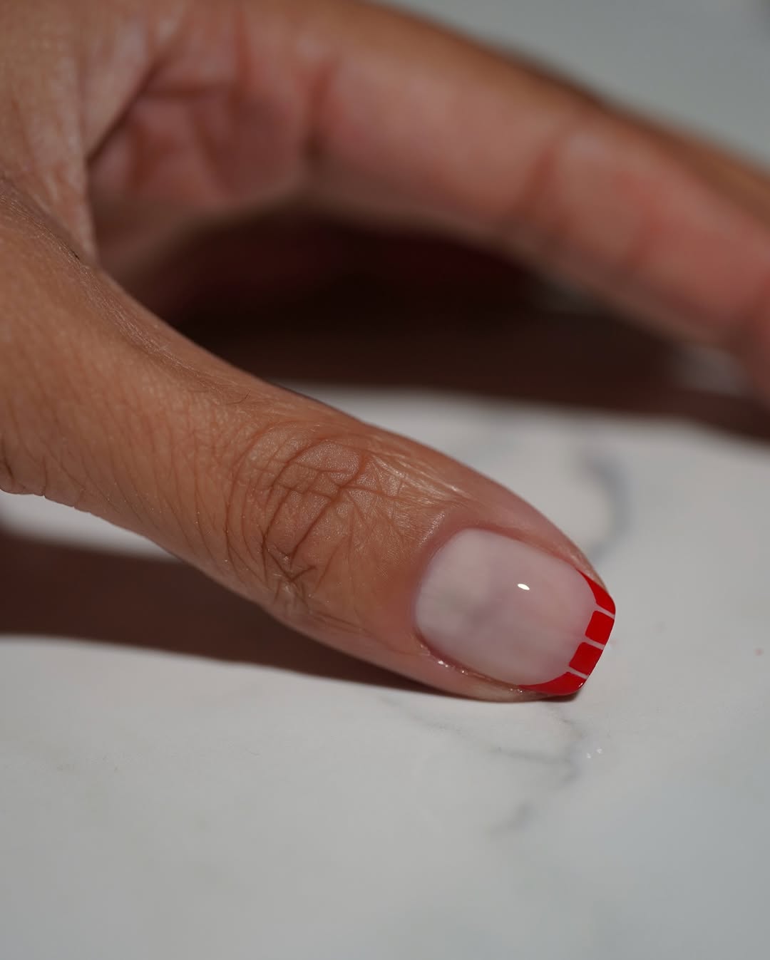 A red manicure with negative space french tip by Iram Shelton