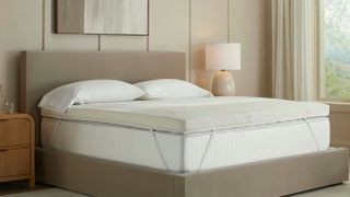 Saatva Graphite Memory Foam Mattress Topper on a mattress with a beige upholstered bed frame