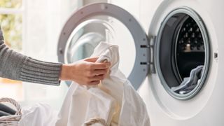 picture of woman putting white sheets in the washing machine