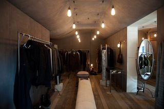 A walk in wardrobe with clothes handing on rails and light bulbs hanging from the ceiling