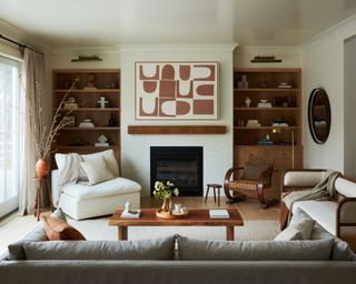 living room with cream armchair, gray sofa, coffee table, bench, rattan chair, fireplace, shelving and artwork