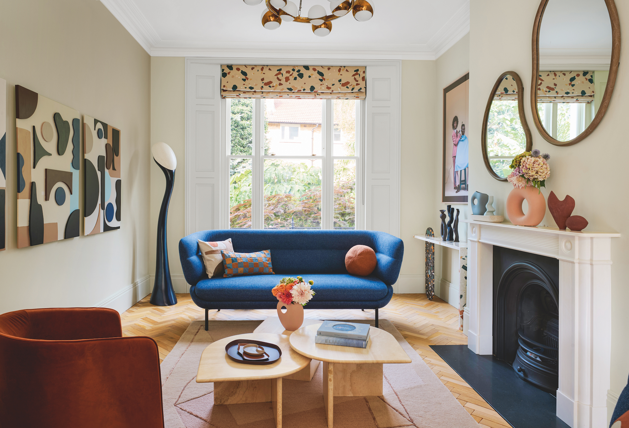 Light living area with a white stone fireplace to the right and a navy blue sofa in front of the bay window, and multiple art pieces on the walls.