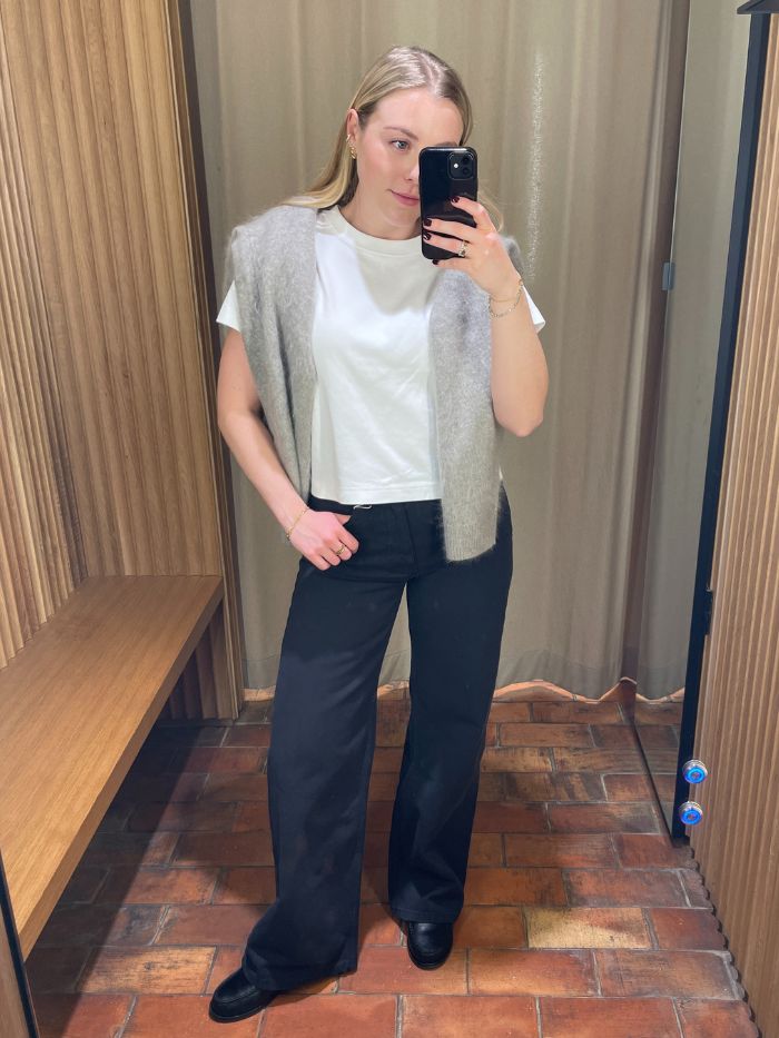 Woman wears white t-shirt, grey jumper over shoulders and black wide-leg jeans