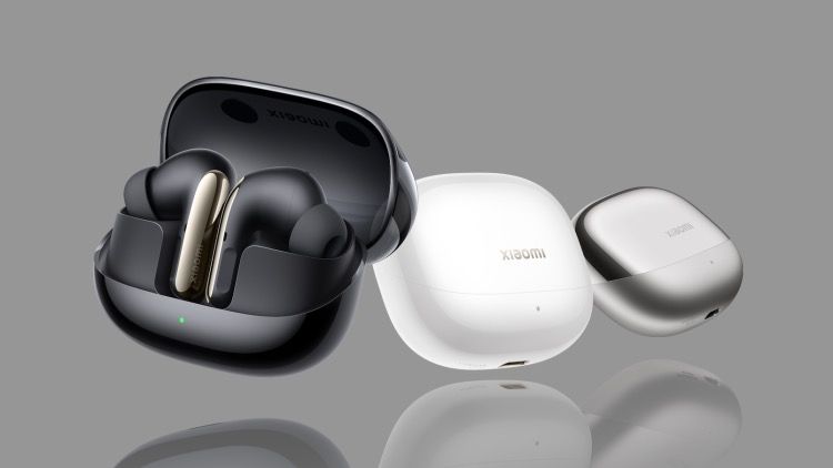 The Xiaomi Buds 5 Pro in a black carry case, next to white and silver carry cases, on a grey background.