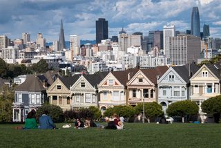 People relax in a park in Alamo Square by the colorful Painted Ladies houses with the San Francisco skyline behind them