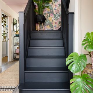 A hallway with a staircase painted black and a pink floral wallpaper on the wall